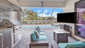 Un amplio espacio exterior con piscina, parrilla y televisor de pantalla plana.