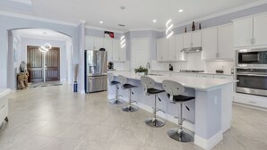 Una cocina moderna con armarios blancos, electrodomésticos de acero inoxidable y una isla central con taburetes de bar.