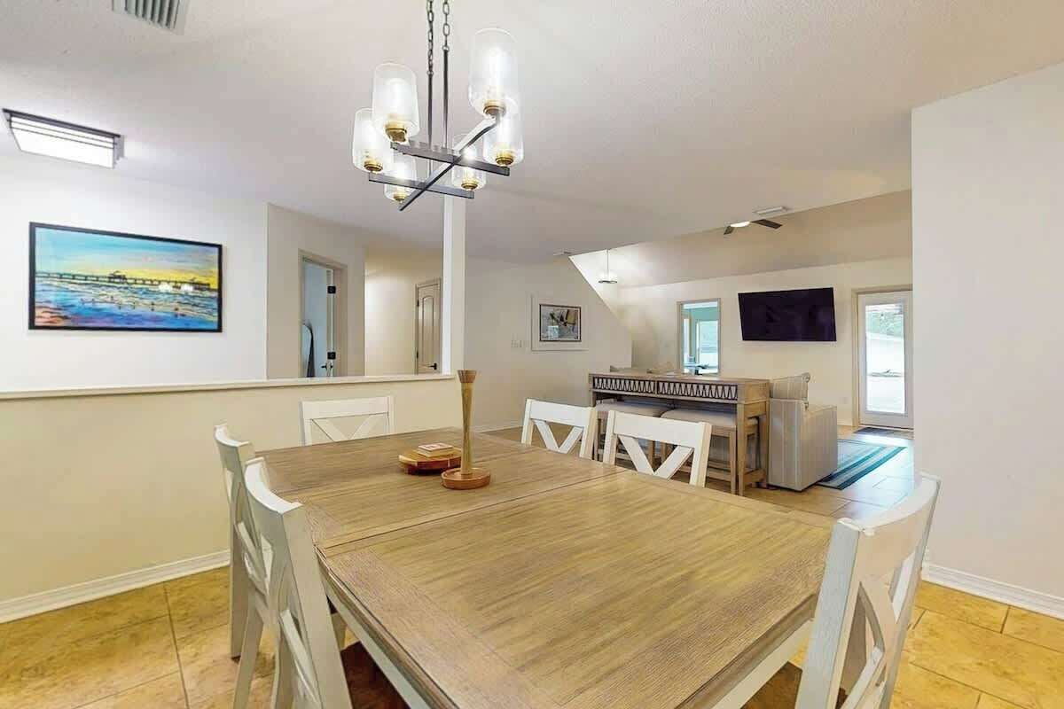 Un comedor con una mesa de madera y sillas blancas, una lámpara de araña y un cuadro en la pared.