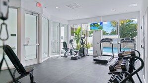 Un gimnasio moderno con máquinas de cardio, bancos de pesas y vista a la piscina.