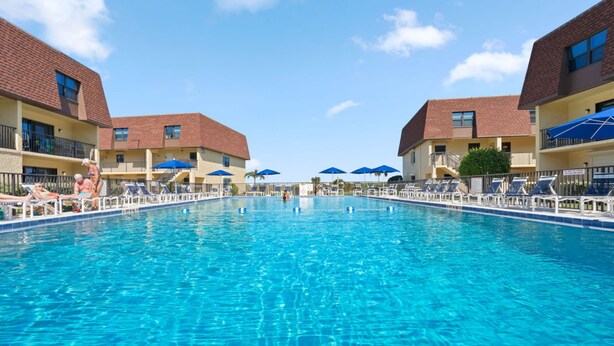 Une piscine entourée de bâtiments dotés de balcons, avec des chaises longues et des parasols à proximité.