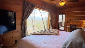 Une chambre dans un chalet en bois, avec un lit, un ventilateur de plafond, une télévision et une fenêtre avec des rideaux.