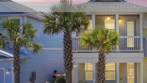 A two-story house with a balcony, surrounded by palm trees and a garden.