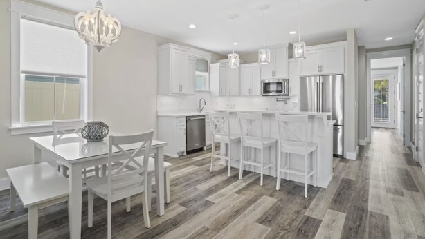 A modern kitchen with white cabinetry, a central island with bar stools, a chandelier, and a view to the outside.