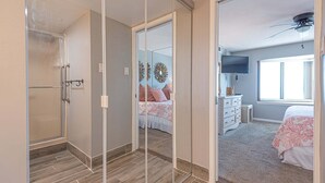 Un dormitorio con un espejo grande, una cama con ropa de cama rosa, un tocador y un ventilador de techo.