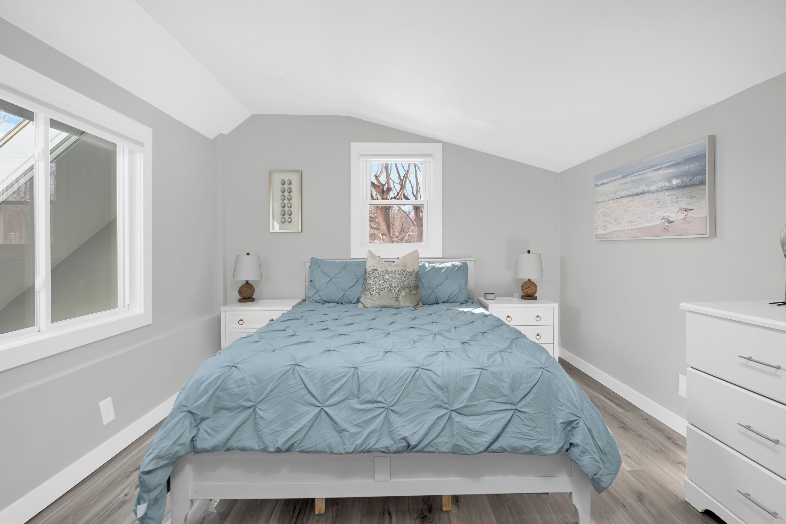 A bedroom with a bed, nightstands, a dresser, a window, and a painting on the wall.