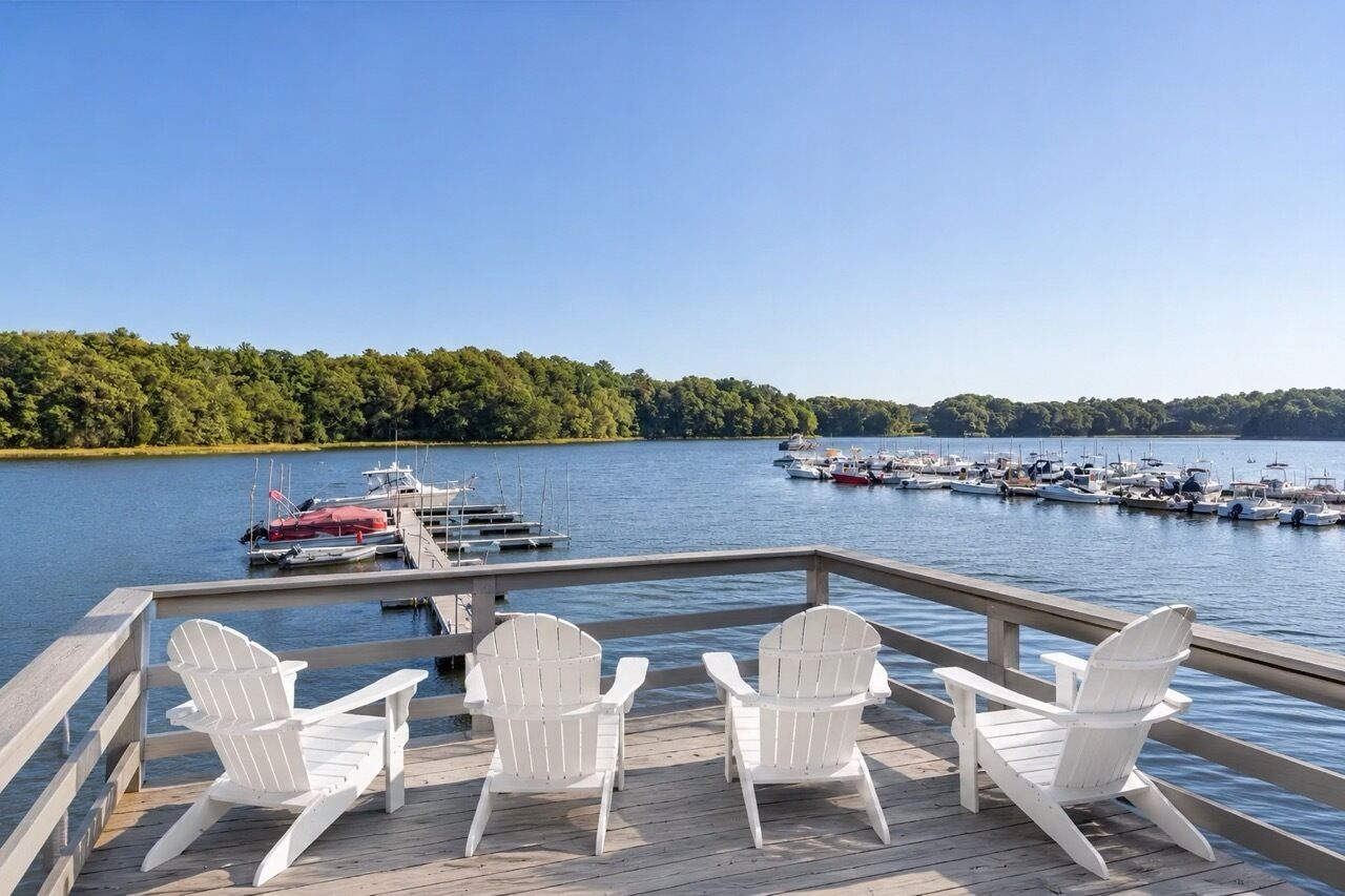 Een steiger met witte Adirondack-stoelen, gericht op een jachthaven met boten.