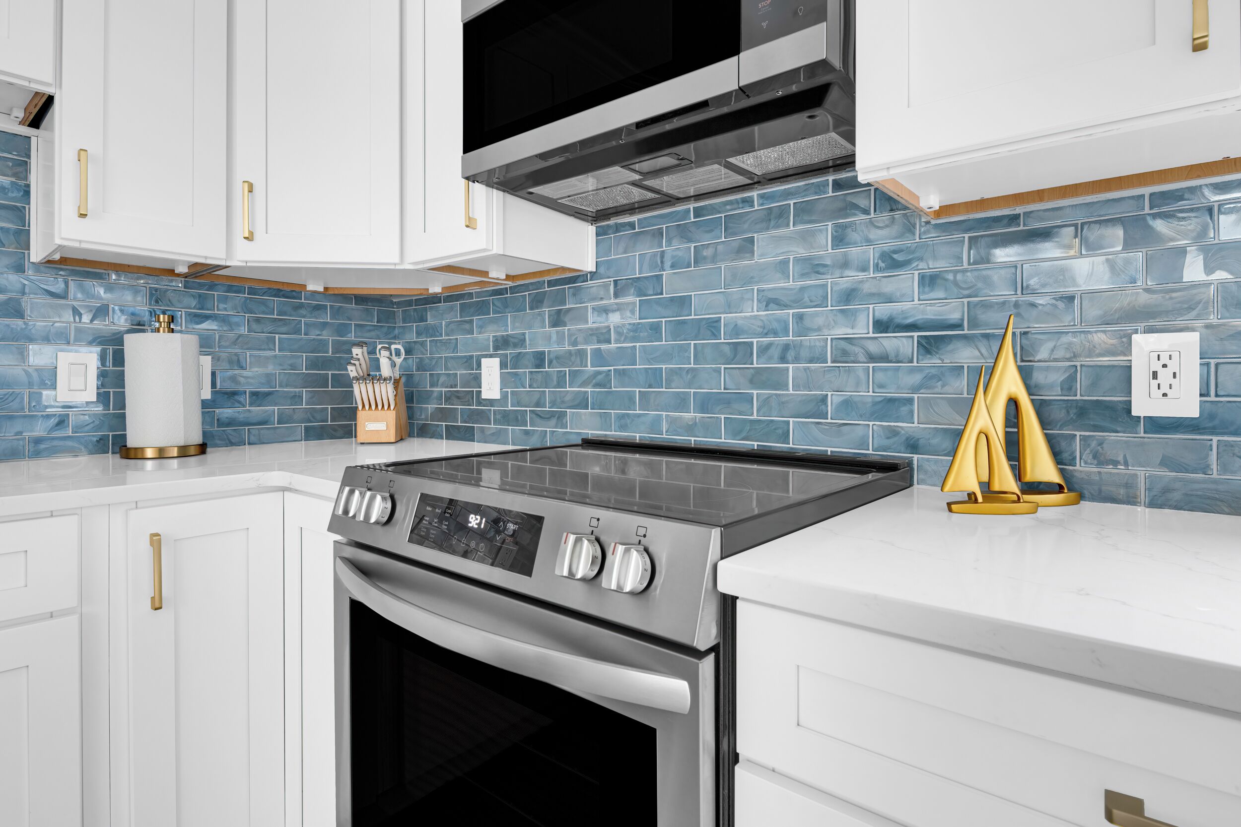 A modern kitchen with white cabinets, a stainless steel stove, and blue-tiled backsplash.