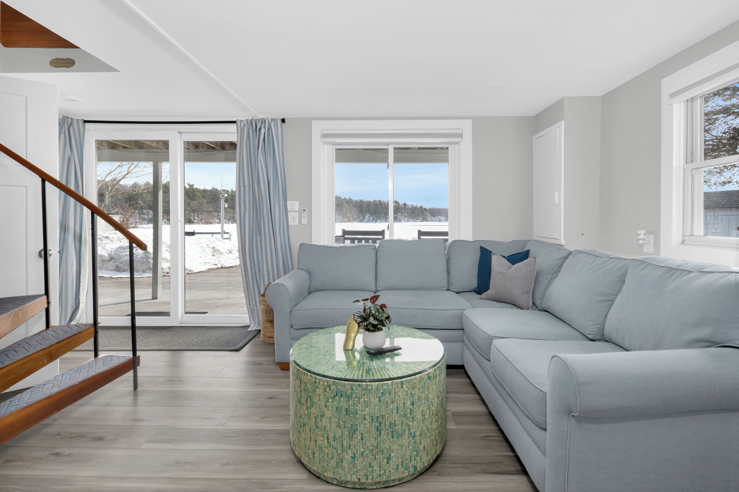 A modern living room with a grey sofa, a round green coffee table, and a wooden staircase.