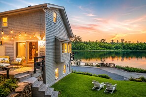 Una casa de dos pisos con un balcón, mobiliario exterior y vista a un lago.
