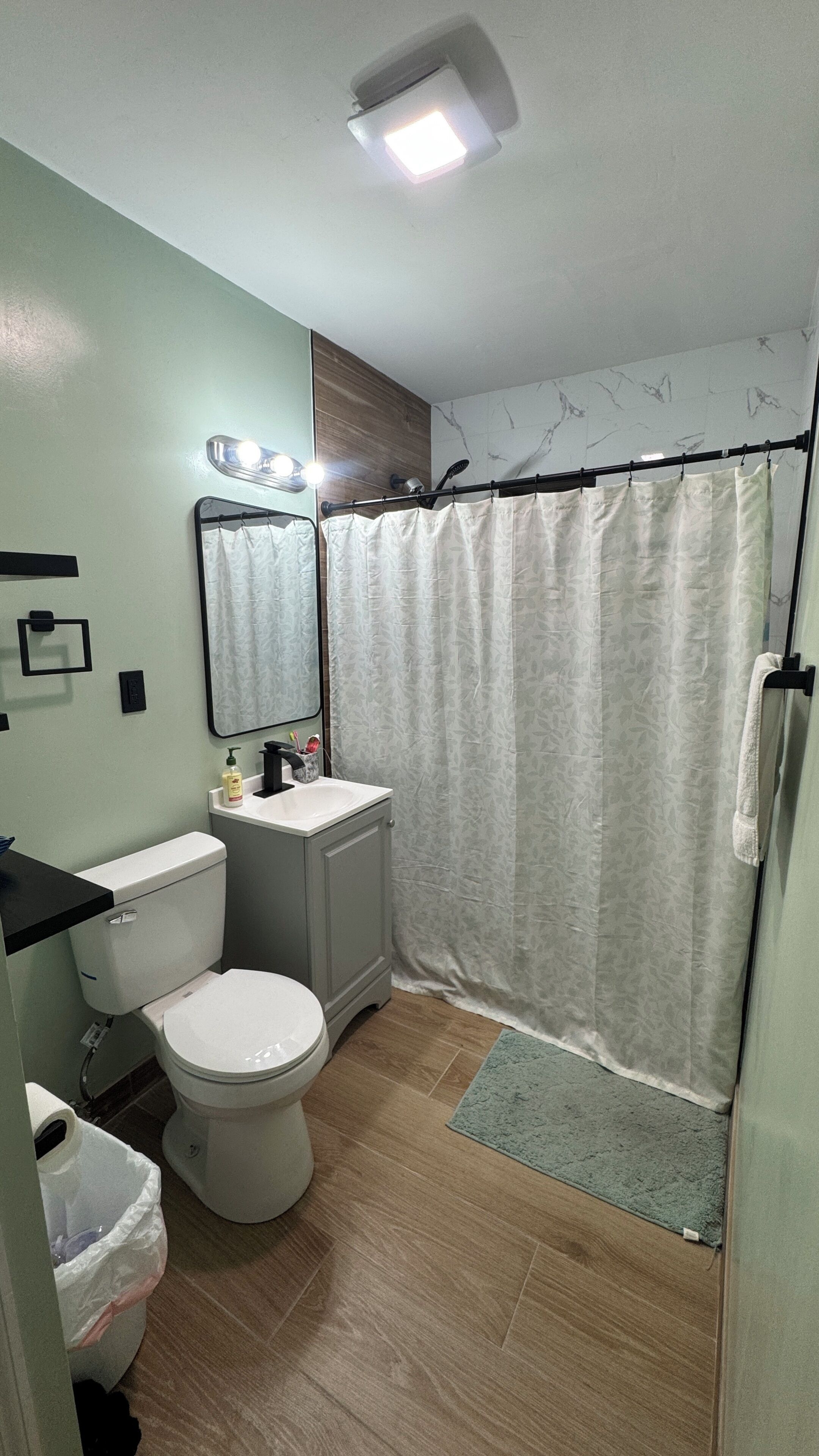 A bathroom with a toilet, sink, mirror, shower curtain, and a light fixture.