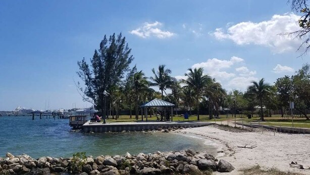 Ein Strand mit einer Laube, Palmen und einem Pier im Hintergrund.