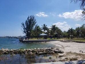 A beach with a gazebo, palm trees, and a pier in the background. - Papaya Cottage - Intercoastal 1 block away (West Palm Beach)