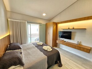 Ein modernes Hotelzimmer mit einem Bett, einem Fernseher, einem kleinen Tisch und einem Balkon.