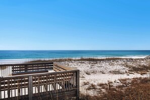 A beach view with a wooden deck and a sandy area with sparse vegetation. - Steps to the Beach Pool  Courts  Family Fun (Destin)
