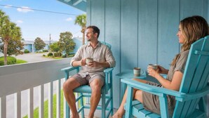 Two people sitting on turquoise chairs on a porch with a view of a residential street. - Steps to the Beach Pool  Courts  Family Fun (Destin)