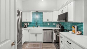 A modern kitchen with white cabinets, a teal backsplash, stainless steel appliances, and a microwave. - Steps to the Beach Pool  Courts  Family Fun (Destin)