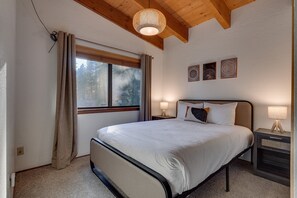 Ein Schlafzimmer mit einem großen Bett, Holzbalkendecke, einem Fenster mit Vorhängen und drei Wandbildern.