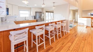 A modern kitchen with wooden flooring, white bar stools, and stainless steel appliances. - The Good Stuff - Oceanfront charmer with direct beach access (Virginia Beach)