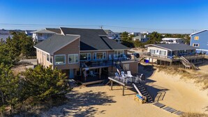 A beachfront property with a large house featuring multiple balconies, a deck, and a staircase leading to a sandy beach area. - The Good Stuff - Oceanfront charmer with direct beach access (Virginia Beach)