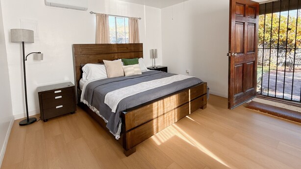 Un dormitorio con cama de madera, mesitas de noche, ventilador de techo y ventana con cortinas.