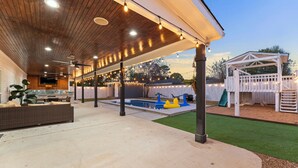 Ein Außenbereich mit Terrasse, Pool, überdachter Sitzgelegenheit und einem Spielbereich.