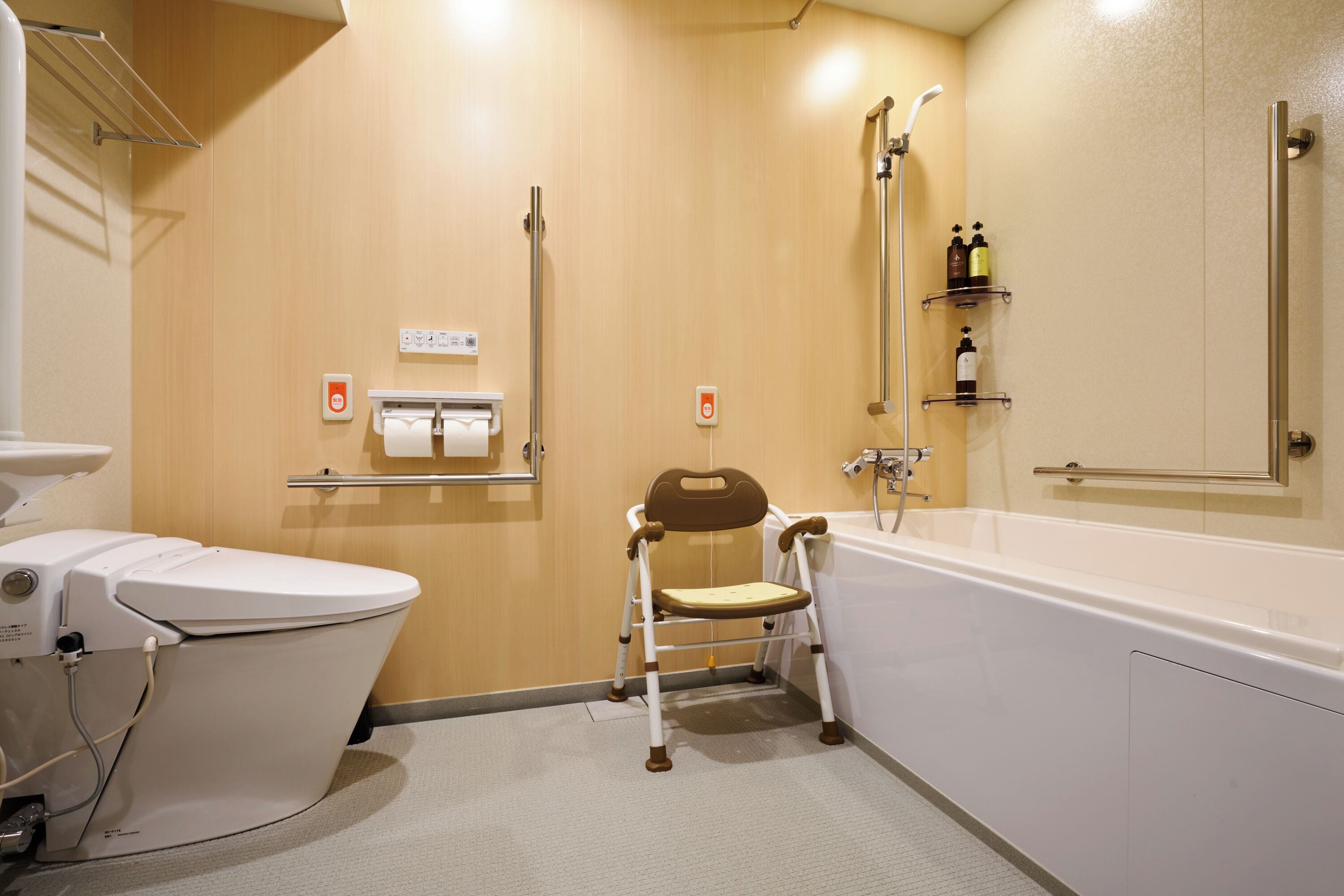 Et badeværelse med toilet, bruser, gelænder og en kørestolsvenlig stol.