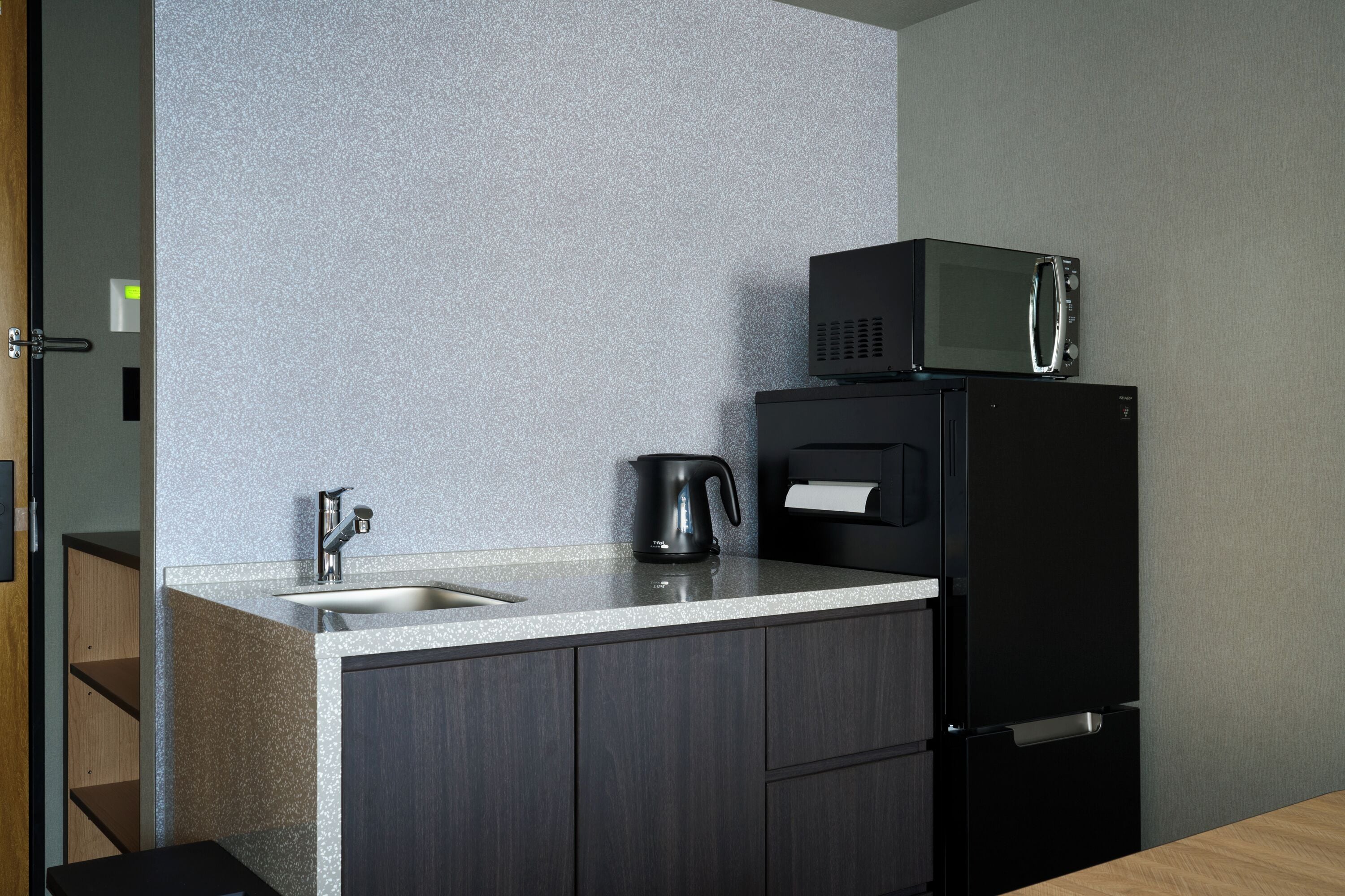 A compact kitchen with a sink, a kettle, a microwave, and a refrigerator.