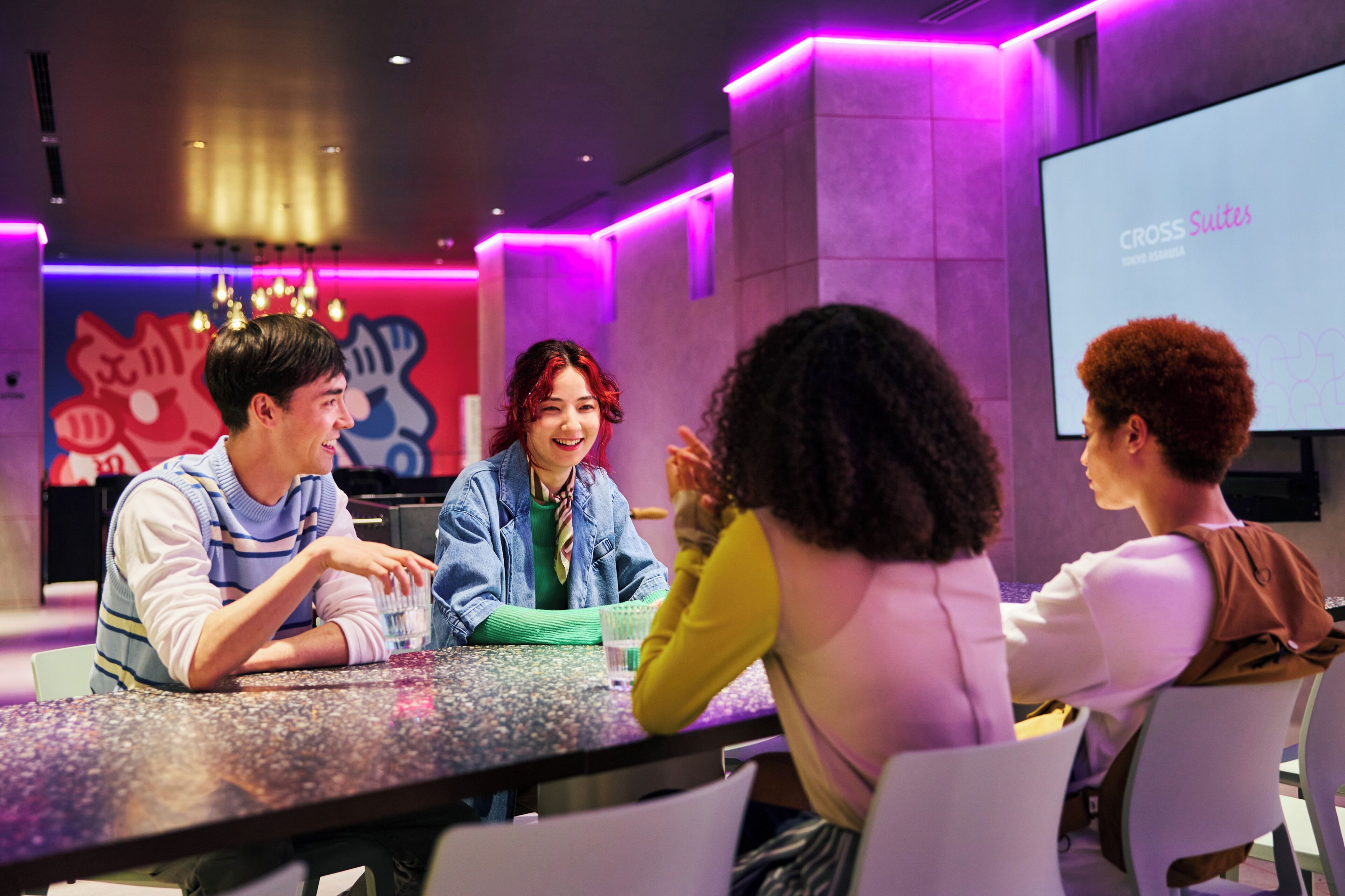 A modern interior with a presentation screen, a table with people, and colorful wall art.