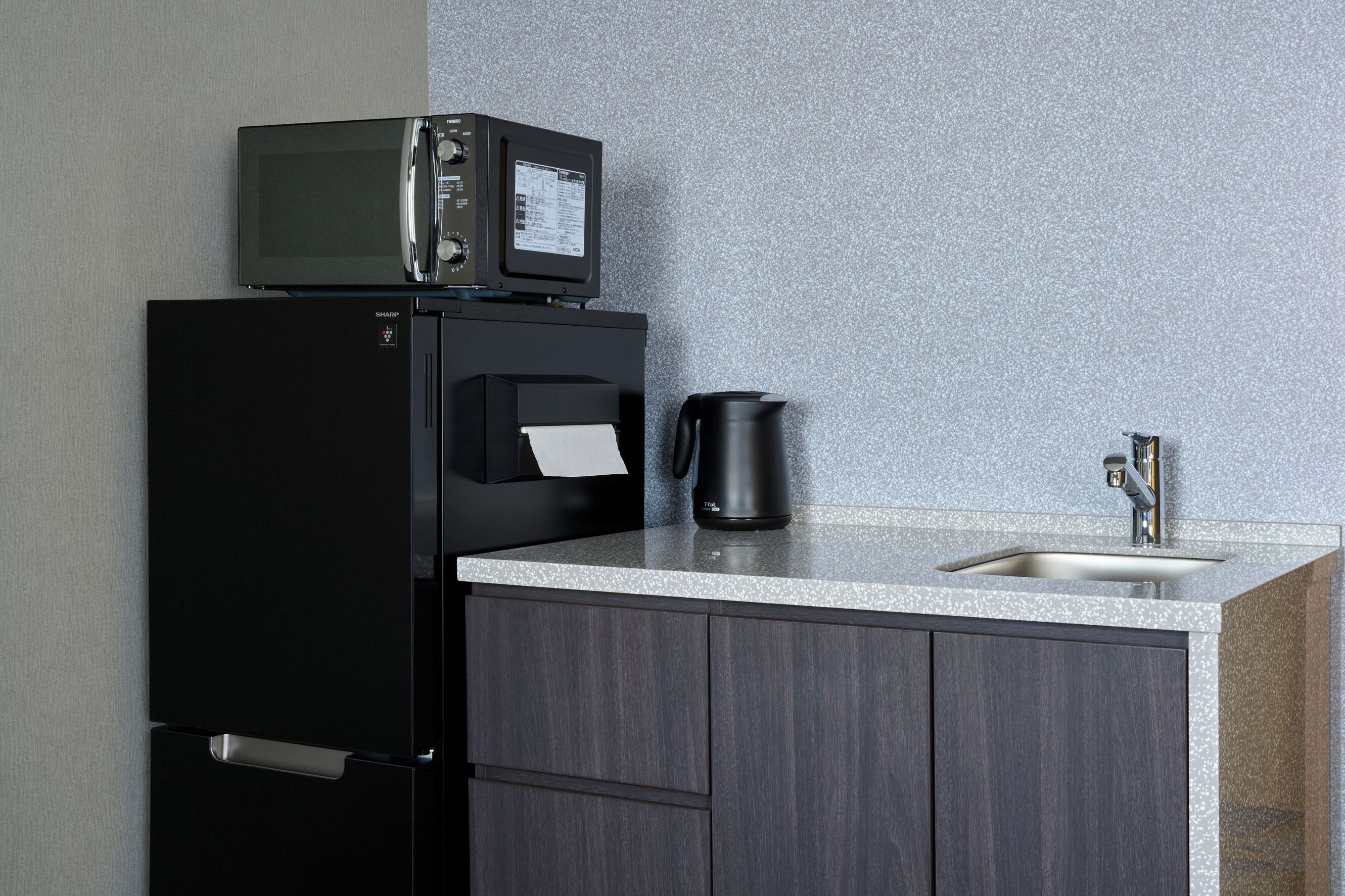 A kitchen with a black refrigerator, a microwave, a coffee maker, and a sink.