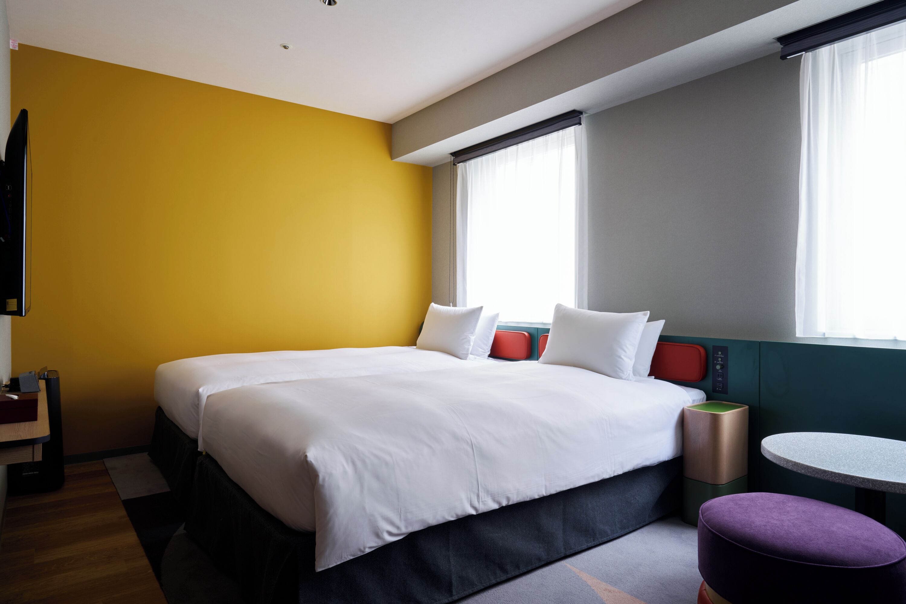 A hotel room with a large bed, a small table, a chair, and a window with curtains.