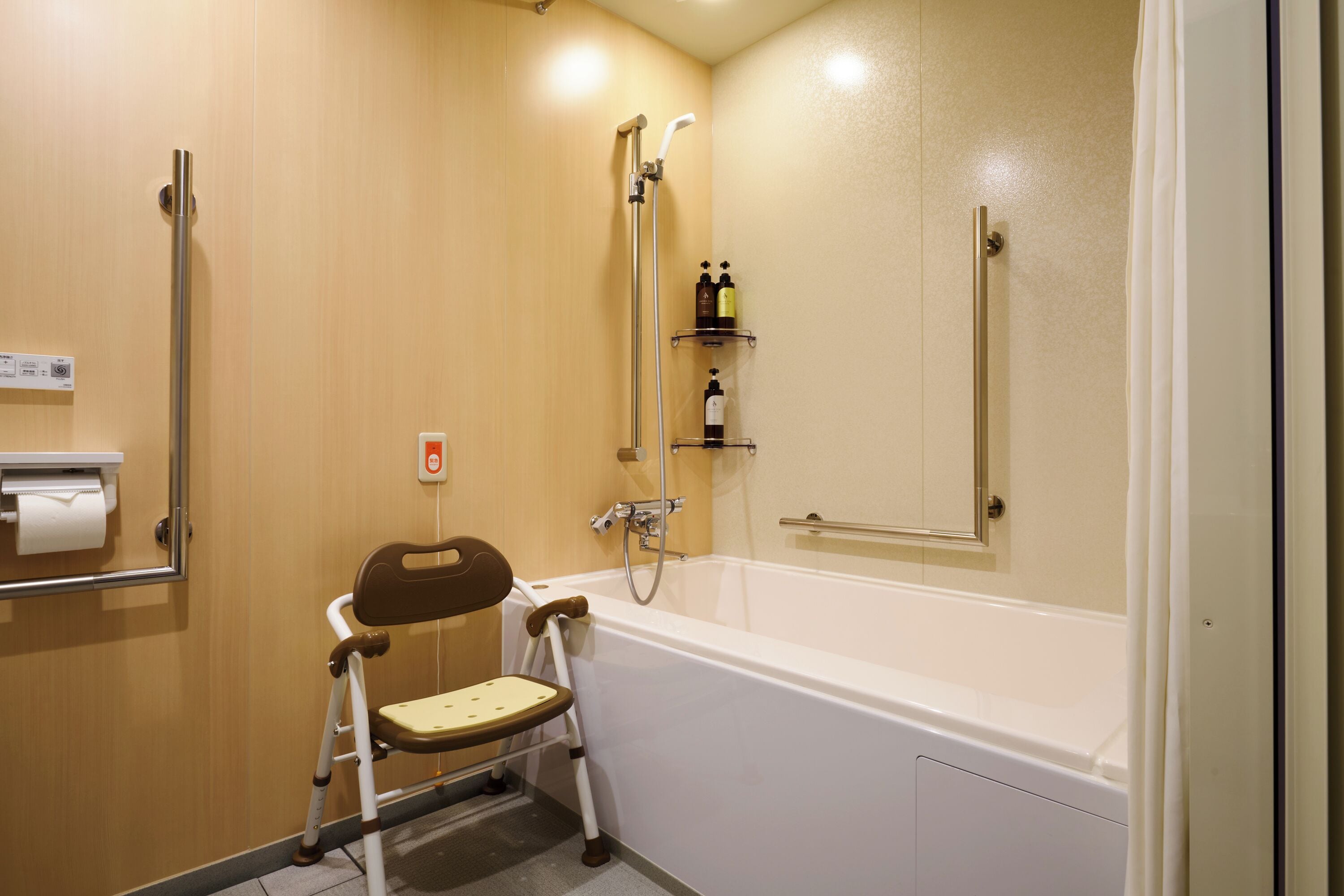 A bathroom with a wheelchair-accessible shower, a toilet paper dispenser, and a handrail.