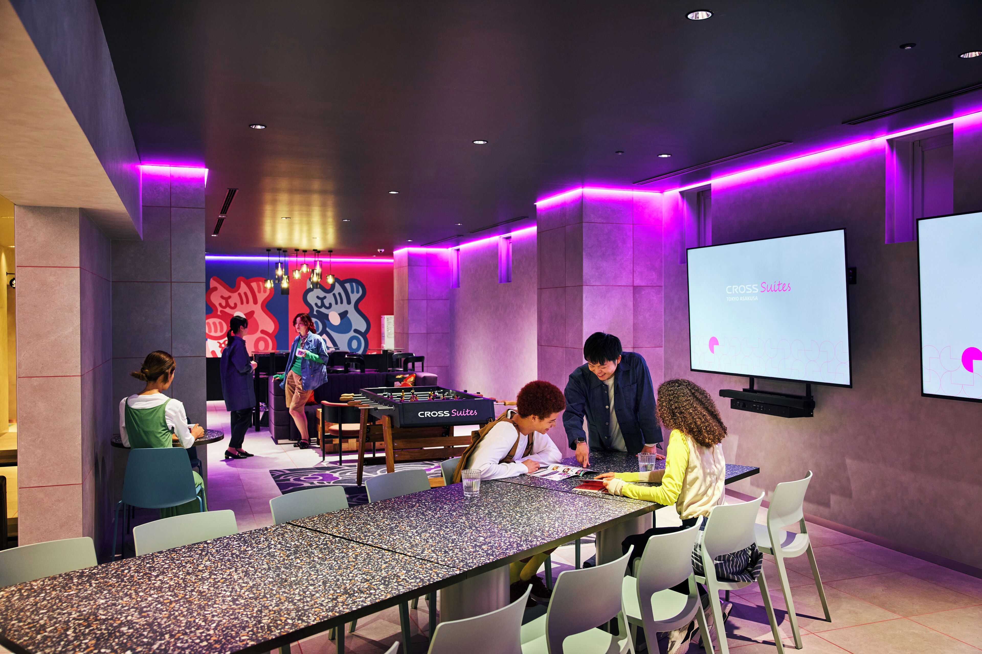 A modern conference room with a foosball table, a large screen, and a group of people engaged in a meeting.