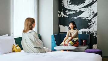 Una habitación con una cama, una mesa redonda, un sofá azul y un cuadro abstracto grande en la pared.