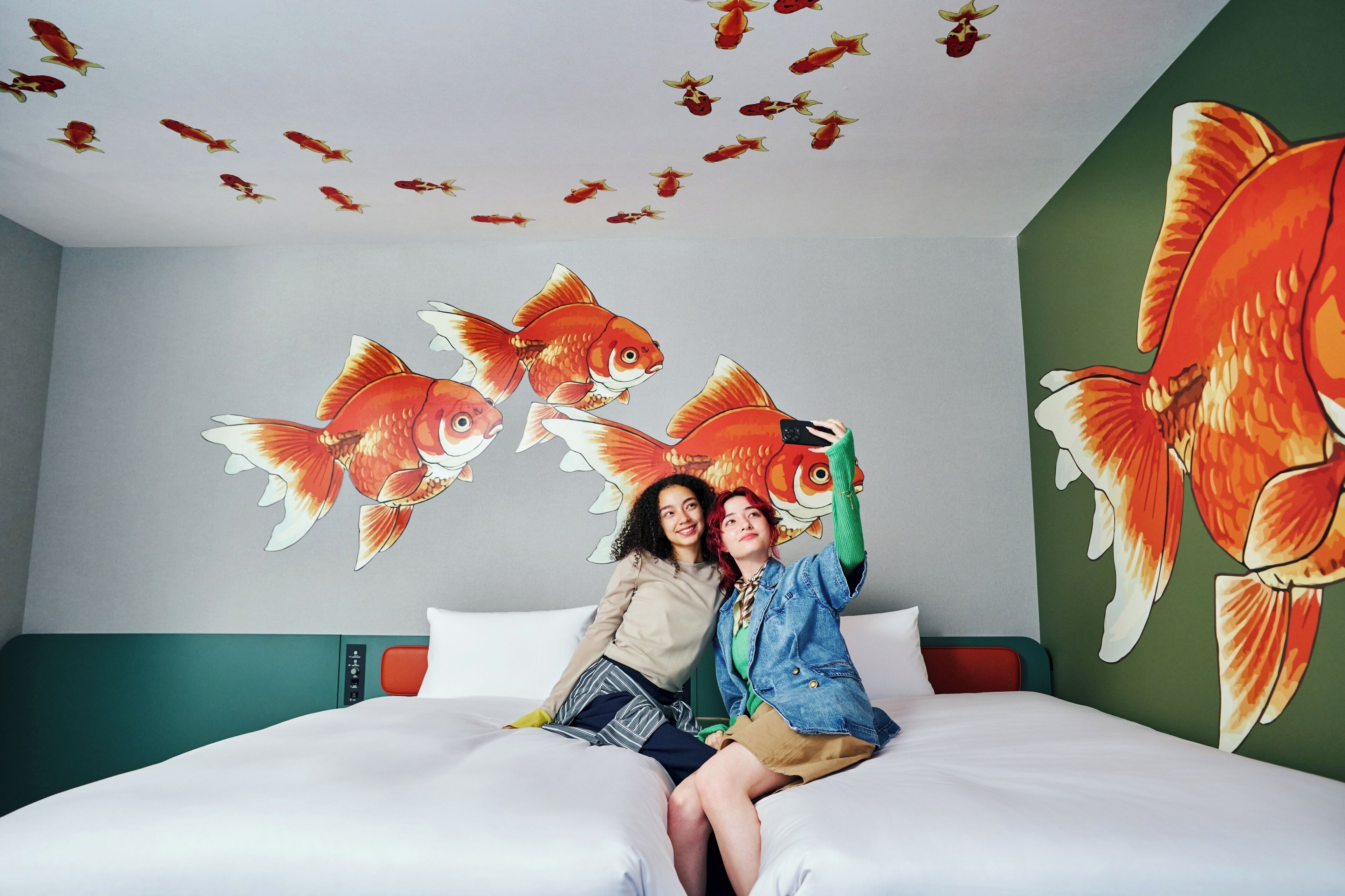Une pièce avec un lit, un mur vert et une fresque représentant des poissons.