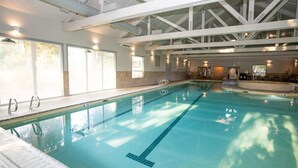 Una piscina interior con carriles claramente delimitados, un techo alto con vigas estructurales visibles y luz natural que entra por amplias ventanas.