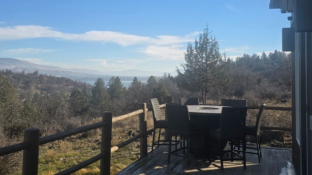 Una terraza de madera con una mesa y sillas, con vista a un paisaje montañoso.