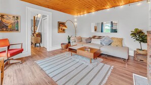 Een moderne woonkamer met een houten plafond, een bank, een salontafel en een gestreept vloerkleed.