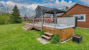Een achtertuin met een jacuzzi, een houten terras en een overdekte patio.