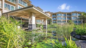 A hotel with a pool surrounded by water lilies and tropical plants, featuring multiple balconies and a modern architectural design. - Waipouli Beach Oceanfront Resort (Kapaa)