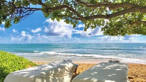 Two beds under a tree on a beach with a view of the ocean. - Waipouli Beach Oceanfront Resort (Kapaa)