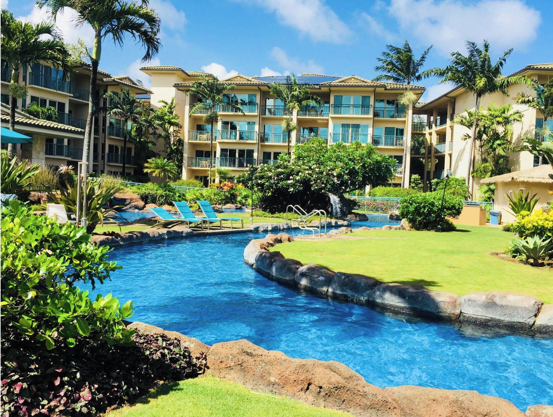 A resort with a swimming pool, lounge chairs, and a multi-story building with balconies.