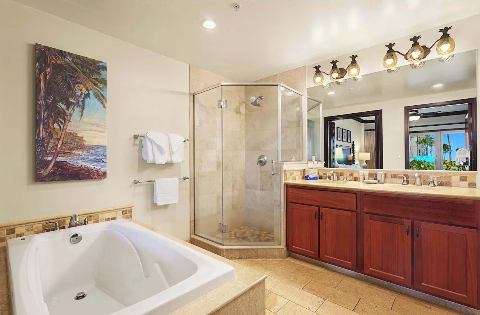 A modern bathroom with a large bathtub, a glass-enclosed shower, wooden cabinets, and a painting of a beach scene.