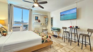 Ein Hotelzimmer mit Bett, Schreibtisch mit Stuhl, Fernseher an der Wand und einem Balkon mit Blick auf die Stadt.