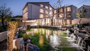 A modern hotel with a large outdoor pool and waterfall, featuring multiple floors and large windows.