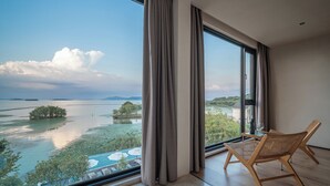 A spacious room with a large window offering a view of a lake and distant mountains.