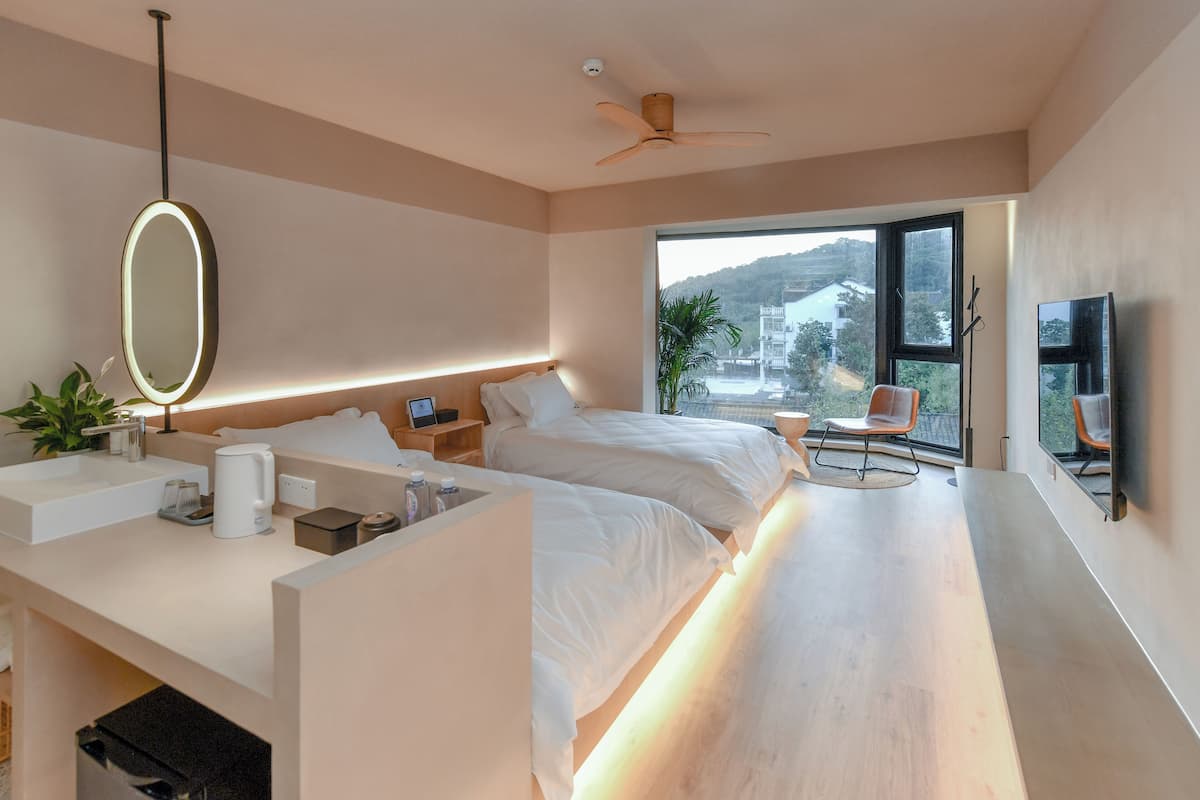 A modern hotel room with a large bed, bedside tables, a desk with a mirror, a flat-screen TV, and a balcony with a view of the city.