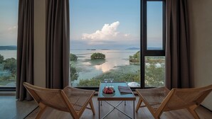 A room with large windows, a table with two chairs, and a view of a lake and distant mountains.