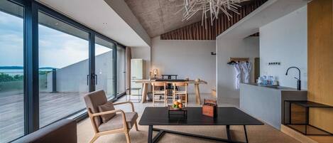 Un intérieur moderne avec une grande baie vitrée, un coin repas avec une table et des chaises en bois, et un espace détente avec des canapés.