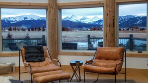 Une pièce dotée de grandes fenêtres donnant sur les montagnes, de deux fauteuils en cuir, d’une petite table ronde et d’un plancher en bois.